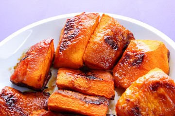 Pumpkin, ultraviolet background, baked pumpkin with honey, white plate with orange vegetables, pop art, slices of pumpkin on purple background, vegetarianism, healthy food, macrophotography
