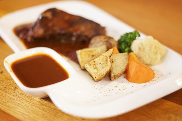 Beef steak with grilled potato in white plate on the wooden table.