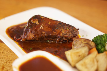 Beef steak with grilled potato in white plate on the wooden table.
