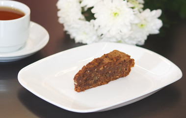 brownie cake on a white plate decorated with chrysanthemum flowers prepared for tea with a mug of tea