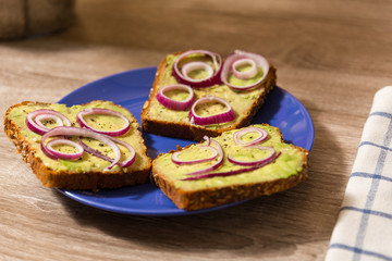 three avocado toast with salt and pepper and red onion cut in rings on a blue plate