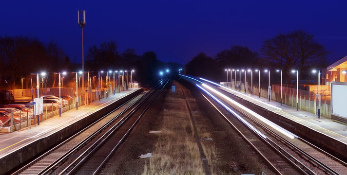 Train passing through a mainline station in southern England, captured at night