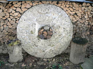 Mühlstein vor einem Stapel Brennholz