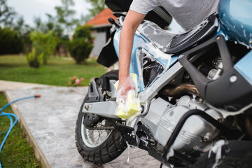 Fototapeta na wymiar A man cleaning motorcycle with sponge, motorcycle detailing (or valeting) concept. Selective focus. 