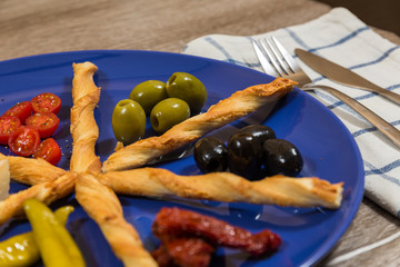 close up of mediterranean antipasti plate with two kinds of olives tomatoes cheese filled peppers separated by breadsticks
