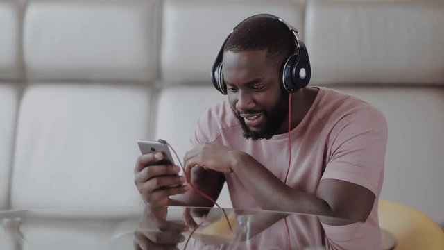 African guy is listening to music enjoying anf looking at his phone