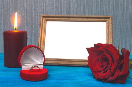 Wedding ring in a gift present box and empty photo frame of a loved one copy space and red rose flower on wooden table background. Marriage offer template. The proposal concept.