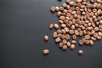 The grains of roasted coffee are scattered on a black matte surface