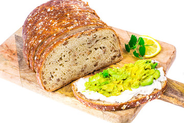 Slice of whole wheat bread with avocado and goat cheese on wooden board