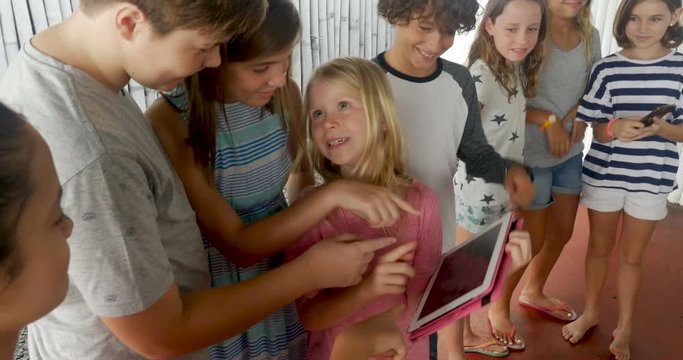 Large group of young boys and girls sharing a tablet and smart phone technology