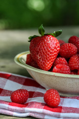 Raspberries with one strawberry inside bowl