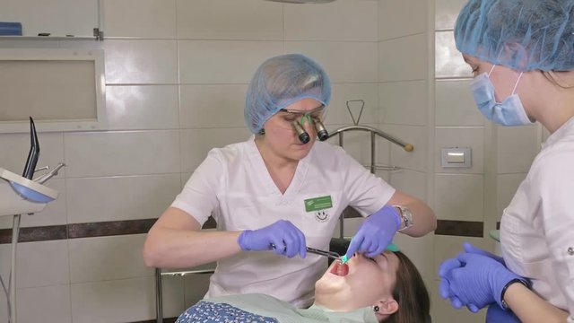 Woman at dentist clinic gets dental treatment to fill a cavity in a tooth. Dental restoration and composite material polymerization with UV light and laser. The doctor works with an assistant.