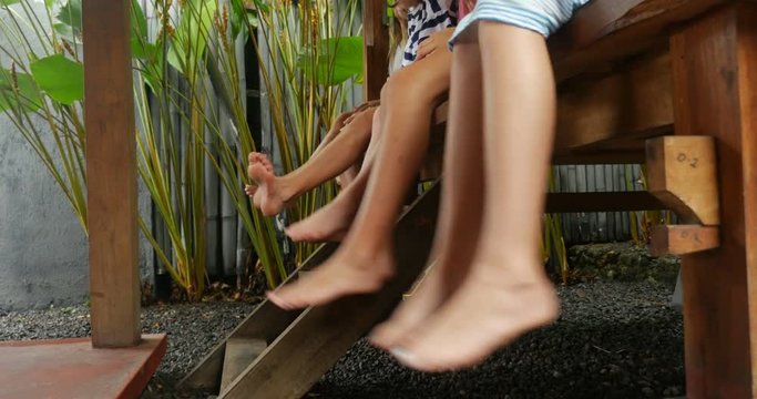 Group of young girls with bare feet swinging their legs while sitting outside