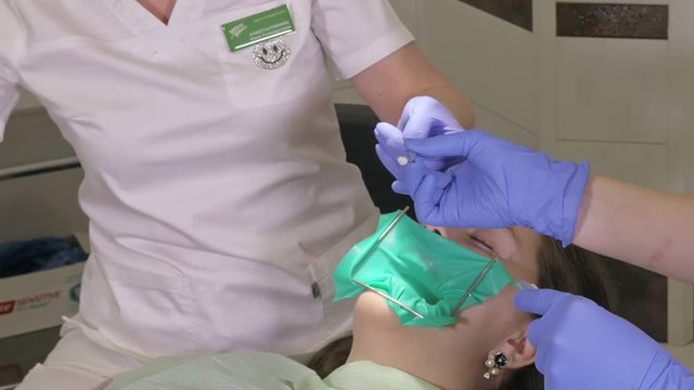 Woman at dentist clinic gets dental treatment to fill a cavity in a tooth. Dental restoration and composite material polymerization with UV light and laser. The doctor works with an assistant.