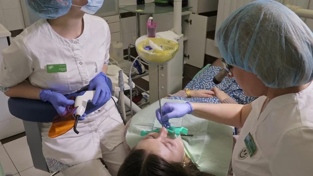 Woman at dentist clinic gets dental treatment to fill a cavity in a tooth. Dental restoration and composite material polymerization with UV light and laser. The doctor works with an assistant.