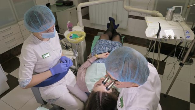 Woman at dentist clinic gets dental treatment to fill a cavity in a tooth. Dental restoration and composite material polymerization with UV light and laser. The doctor works with an assistant.