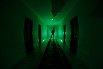 Creepy silhouette in the dark abandoned building. Dark corridor with cabinet doors and lights with...