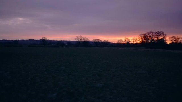 landscape view of grass, field and silhouettes of trees with dramatic sun rising dawn. Camera panning