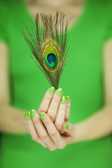 woman hand holding exotic peacock feather, sensual studio shot with green background