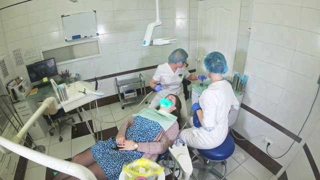 Woman at dentist clinic gets dental treatment to fill a cavity in a tooth. Dental restoration and composite material polymerization with UV light and laser. Shooting at a wide angle.