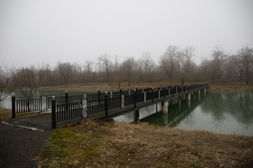 Amazing landscape of bridge reflect on surface water of lake, fog evaporate from pond make romantic scene or Beautiful bridge on lake with trees at fog.