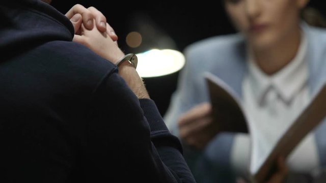 Handcuffed murderer feeling guilty at interrogation meeting with strict agent