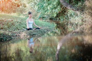 Fototapeta na wymiar Front view of woman meditating in a lotus yoga position at the rill in the forest
