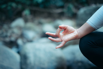 Yoga concept. woman hand practicing lotus pose sitting on the rock at tropical brook in forest