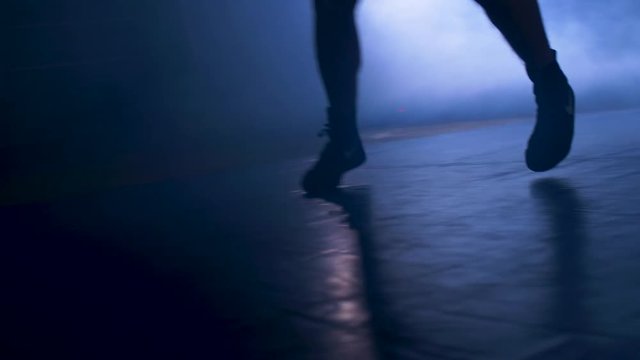 Bottom view of fighter training in the gym with smoke and light background. Silhouette of strong male boxer on dark background. Close up of athlete or sportsman moving fast while training