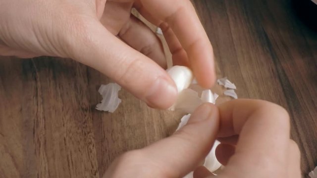 Peeling off skin from garlic clove on wooden tabletop background. Woman hands prepare food.