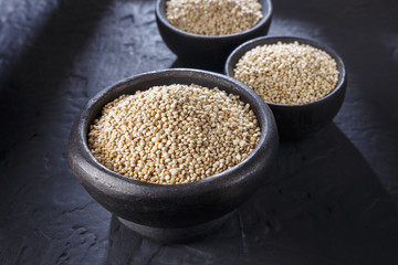 Quinoa grains with spoon and bowl on black background