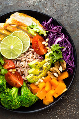 Buddha bowl meal with chicken fillet, brown rice, avocado, pepper, tomato, broccoli, red cabbage, chickpea, fresh lettuce salad, pine nuts and walnuts. Healthy balanced eating. Overhead view
