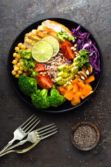 Buddha bowl meal with chicken fillet, brown rice, avocado, pepper, tomato, broccoli, red cabbage, chickpea, fresh lettuce salad, pine nuts and walnuts. Healthy balanced eating. Overhead view