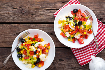 Fresh vegetable salad bowls of tomatoes, corn, pepper, olives, celery, green onion and feta cheese. Healthy food. Diet dinner or lunch menu. Salad plate on table. Flat lay. Top view