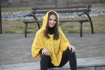 Pretty girl in a yellow handmade knitted poncho sitting on the s