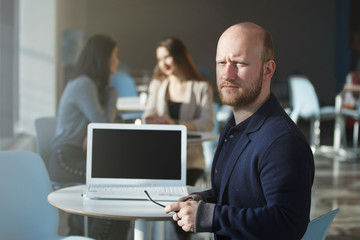 Portrait of happy businessman using laptop and colleagues standing behind and discussing in office