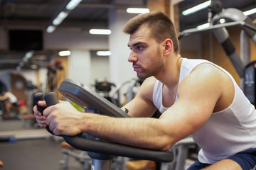 Fitness man on bicycle doing spinning at gym. Fit young man working out on gym bike.