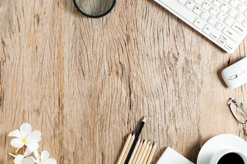 business objects of keyboard,mouse,white coffee cup,white paper,pencils,glasses,magnifying glass and frangipani flowers on old wooden table background.