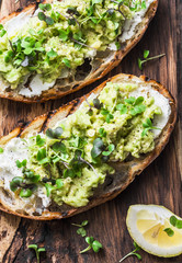 Avocado, cream cheese toast with micro greens on a rustic wooden board, top view. Good fats healthy...