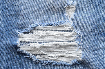 Jeans in wash blue with rip. Denim background, texture. Ripped destructed detail, close up.