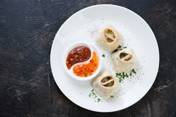 White plate with manti or steamed meat dumplings on a dark brown stone background, view from above, horizontal shot