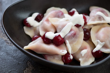 Close-up of boiled vareniki with cherry stuffing and sour cream served in a black bowl, selective focus, horizontal shot