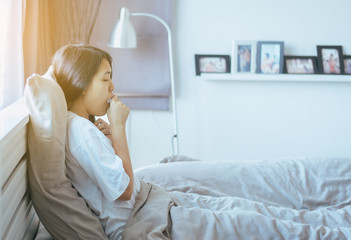 Patient woman coughing and sitting on her bed,Concept of health