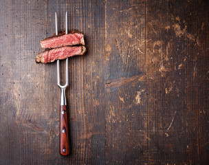Tranches de steak de boeuf sur fourchette à viande sur fond de bois foncé