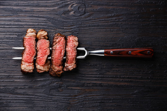 Slices of grilled meat barbecue steak Rib eye on meat fork on burned black wooden background