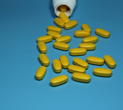 Yellow color Pills scattered on blue background and white pharmacy bottle