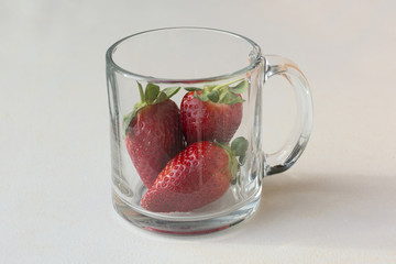 three beautiful red, ripe and delicious strawberries in a glass coffee cup