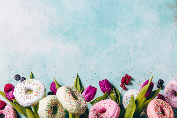 Sweet and colourful doughnuts with sprinkles, purple tulips and berries