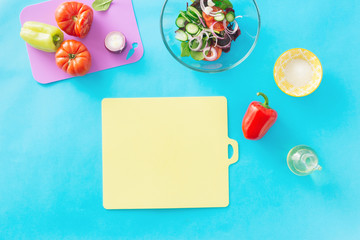 Empty kitchen cutting board with set ingredients for cooking summer salad on blue background, top view. Healthy food concept. Diet food