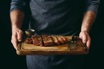 Gartenposter Man holding juicy grilled beef steak with spices on cutting board © kucherav